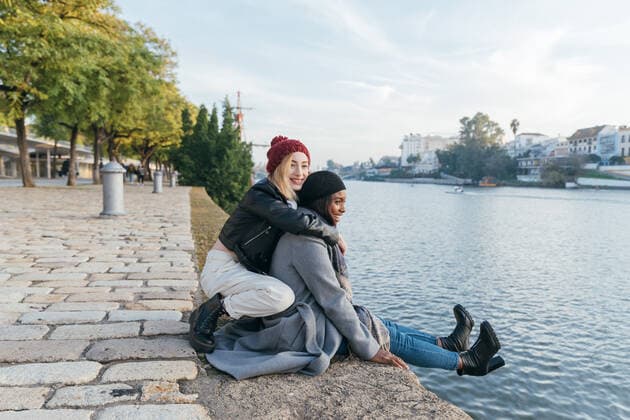 Side view of cheerful multiethnic female friends hugging on promenade while enjoying weekend together in autumn and looking away, Model released Copyright: xJulioxRodriguezx MR