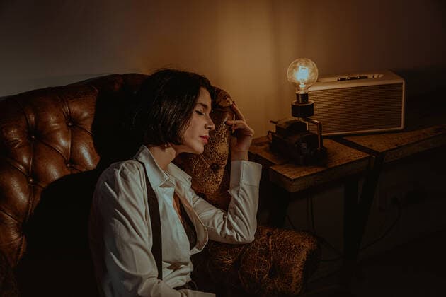 IMAGO Creative: Kulturelle Folgen der Pandemie: Gesundheitsbewu?tsein und Alleinsein Side view of serene female relaxing in old leather armchair in vintage room with glowing light bulb and closed eyes Copyright: xMartaxMartinezx Model Released