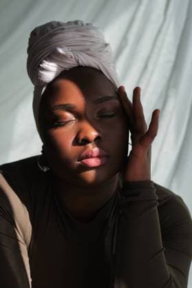 Creative Highlights Symbolbilder Graceful young overweight African female in traditional turban touching face with closed eyes in sunlight, Model released Copyright: xPhilippexDegrootex MR