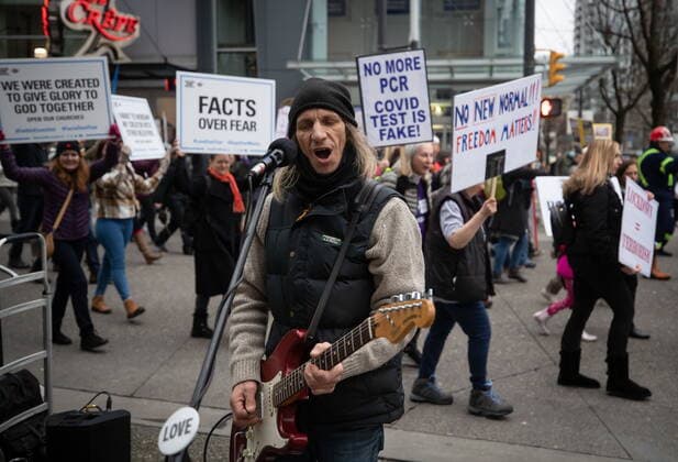 February 20, 2021, Vancouver, BC, Canada: A street performer sings as people opposed to public health measures to curb the spread of COVID-19 march past behind him after the B.C. Grand Freedom Rally, in Vancouver, on Saturday, February 20, 2021. Vancouver Canada  - ZUMAc35_ 20210220_zaf_c35_026 Copyright: xDarrylxDyckx