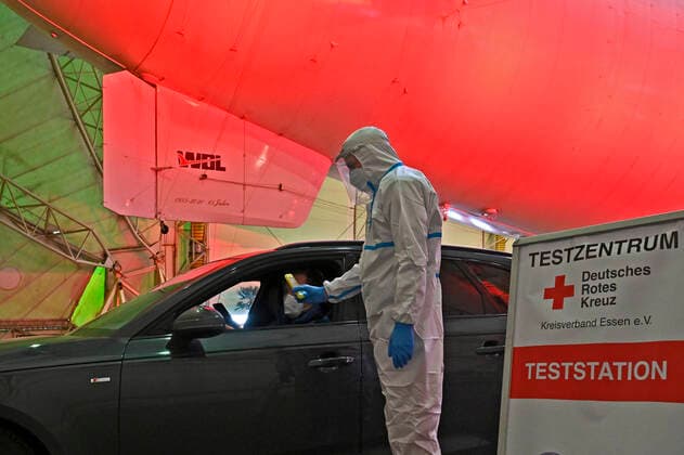 19.02.21, Essen-Muelheim, Nordrhein-Westfalen, Ruhrgebiet, Deutschland. Antigen-Schnelltest im Luftschiffhangar am Flughafen Essen-Muelheim. Buerger, die einen Schnelltest machen moechten, koennen online einen Termin vereinbaren und nach Wunsch einen Nasen-Rachentest oder Spucktest machen lassen. Ehrenamtliche Mitarbeiter des DRK entnehmen dann die Proben direkt und werten diese vor Ort aus. Nach 15 Minuten Wartezeit werden die Getesteten per App ueber das Ergebnis informiert. Blick in den Luftschiffhangar. Mitarbeiter des DRK im Schutzanzug erfasst die Daten einer Testperson am Auto. Corona Schnelltest am Flughafen Essen-Muelheim