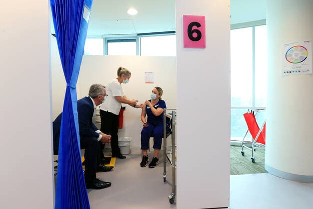 VIC COVID19 VACCINE ROLLOUT, Covid screening nurse Grace Gibney (right) receives one of the first Pfizer coronavirus vaccines from Nurse practitioner Sonja Elia as Health Minister Martin Foley (left) watches on at Austin Health in Melbourne, Monday, February 22, 2021. Australia will begin its roll out of the Pfizer coronavirus vaccine on Monday, the country s most complicated logistical exercise to date. ( NO ARCHIVING, EDITORIAL USE ONLY, NO USE IN BOOKS WITHOUT CONSENT MELBOURNE VIC AUSTRALIA Copyright: xMARKxSTEWARTx 20210222001522293431