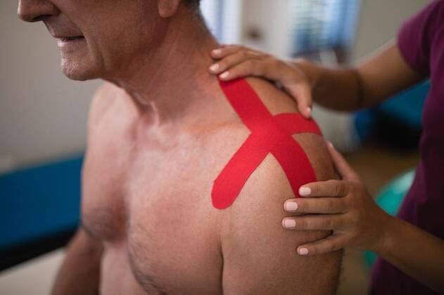 Midsection of female therapist applying elastic therapeutic tape on shoulder Midsection of female therapist applying elastic therapeutic tape on shoulder at hospital ward, model released, , property released, Cape Town, South Africa, 23.04.2017, 1034626.jpg, physiotherapy, physical therapy, medical clinic, healthcare, alternative therapy, care, hospital, examination room, ward, lifestyle, patient, recovery, treatment, therapist, physiotherapist, doctor, support, healing, female doctor, multi-ethnic group, practitioner, specialist, health service, expertise, healthcare worker, millennial, occupation, service occupation, profession, therapy, muscle retraining, touching, bandage, shirtless, sitting, elastic therapeutic tape, elastic tape, tap
