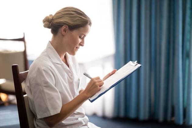 IMAGO Creative: Zivildienst und ehrenamtliches Engagement Side view of young female doctor writing on clipboard Side view of young female doctor writing on clipboard at retirement home, model released, , property released, Cape Town, South Africa, 2017-04-27T23:00:00.000Z, 1041674.jpg, retirement community, nursing home, geriatrics, healthcare and medicine, smiling, sitting, holding, curtain, doctor, female doctor, stethoscope, practitioner, lab coat, specialist, healthcare, health service, expertise, profession, file, document, furniture, millennial, white, hair bun, clipboard, notepad, writing, pen, chair 20s, Young Adult, Woman, Female, Caucasian, 25-29 Years, Young Women, Caucasian Ethnicity Indoors,Side view,Focus on Foreground,Day,Three Quarter Length