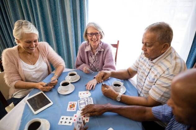 High angle view of senior friends playing cards High angle view of senior friends playing cards while having coffee at table in nursing home, model released, , property released, Cape Town, South Africa, 2017-04-27T23:00:00.000Z, 1042002.jpg, drinking, cup, beverage, coffee, holding, nursing home, retirement community, lifestyle, friendship, active seniors, casual clothing, enjoyment, refreshment, relaxation, retirement, togetherness, playing, competition, smiling, strategy, mobile phone, technology, communication, sitting, geriatrics, multi-ethnic, active, golden years, happy, cards, assisted living, healthcare and medicine 70s, Senior, Elderly, Man, Male, Black, 60s, Mixed-Race, Woman, Female, Caucasian, Senior Men, African Ethnicity, 65