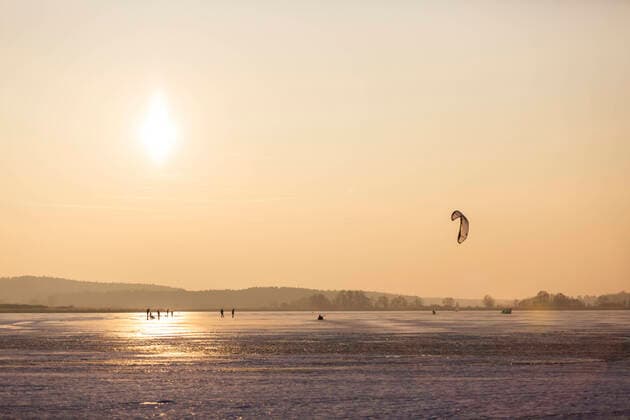 IMAGO Creative: Alternativer Wintersport Germany, Brandenburg, Rangsdorf, Winter landscape with frozen lake, people playing with kite ASCF01536