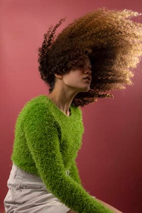 IMAGO Creative: Clickbait, Modetrends Young woman tossing hair while sitting by colored background model released Symbolfoto AXHF00104