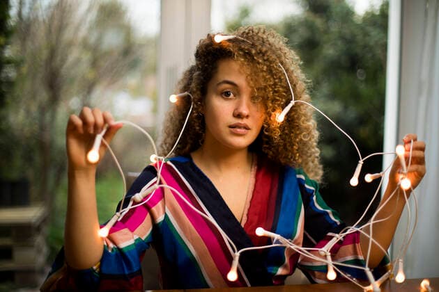 Confused curly haired woman holding illuminated Christmas lights at home model released Symbolfoto property released AXHF00145