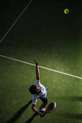 Male athlete servicing ball while playing padel tennis in sports court at night model released Symbolfoto DAMF00670