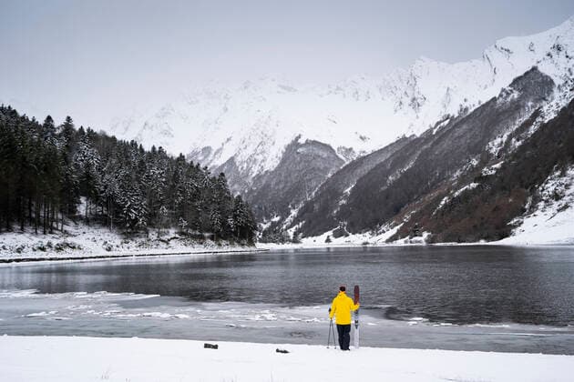 Man with ski at snow covered lakeshore in front of mountains model released Symbolfoto DAMF00684
