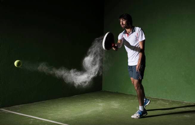 Male athlete servicing ball while playing padel tennis in sports court at night model released Symbolfoto DAMF00672