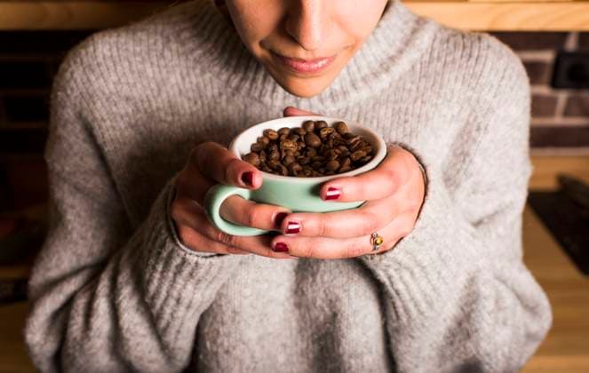 Young woman smelling fresh coffee beans in cup at cafe model released Symbolfoto DAMF00717