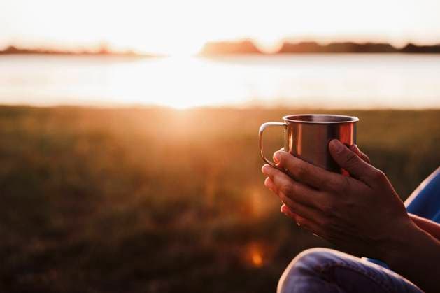 Hands of mid adult woman holding drink against lake during sunset model released Symbolfoto EBBF02205