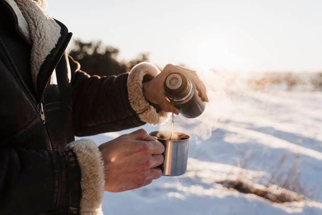 Man pouring hot coffee in cup through thermos on sunny day model released Symbolfoto EBBF02387