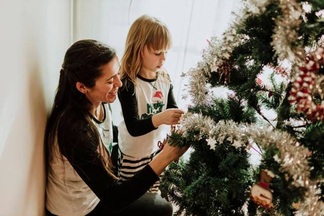 Mother with daughter decorating Christmas Tree against wall at home model released Symbolfoto property released GMLF00956