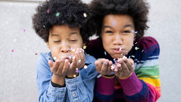 Playful brother and sister blowing confetti while playing against wall model released Symbolfoto JCCMF00981