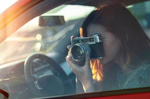 Young woman photographing through old-fashioned camera from car while travelling model released Symbolfoto JMPF00868