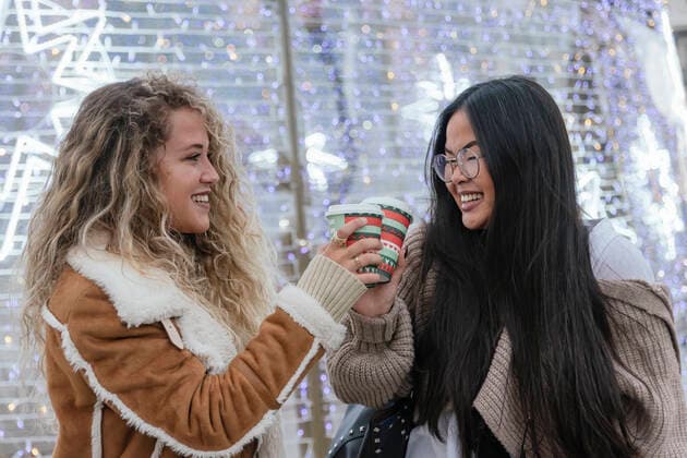 Diversity, Weihnachten Beautiful female friends toasting coffee cups against illuminated Christmas lights model released Symbolfoto JRVF00244