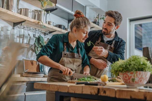 Young chef smelling parsley while cutting scallions standing by colleague on kitchen island model released Symbolfoto property released MFF06987