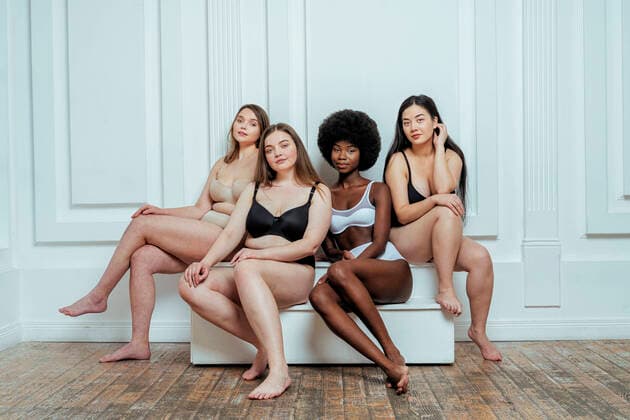 Confident multi-ethnic group of models in lingerie sitting against white wall model released Symbolfoto property released OIPF00219
