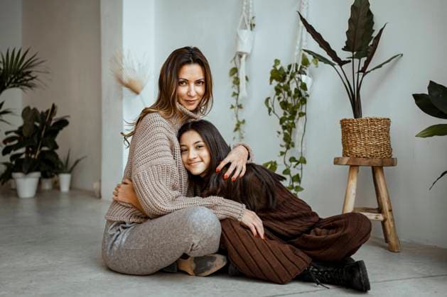 IMAGO Creative: Mutterschaft Smiling daughter embracing mother while sitting by potted plant at home model released Symbolfoto property released RCPF00669