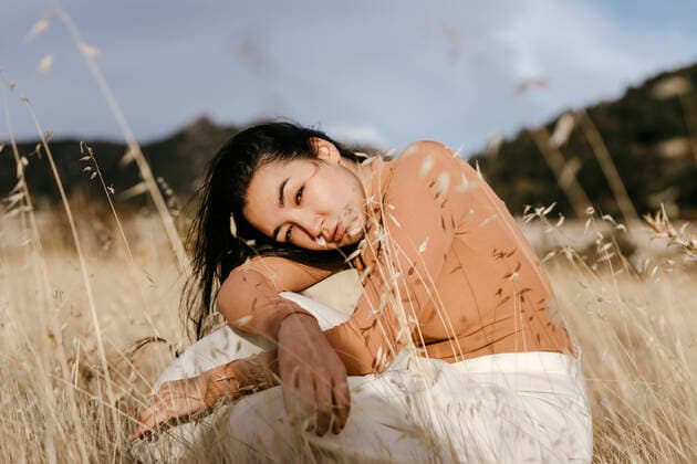 Young woman sitting amidst grass in field against sky during sunset model released Symbolfoto TCEF01433