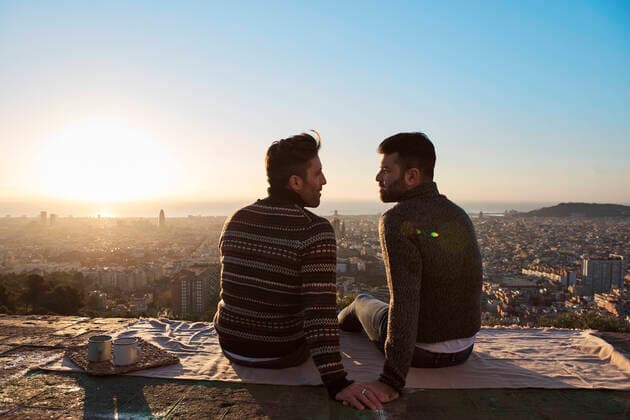IMAGO Creative: Urban Diversity Gay couple looking at each other while sitting on observation point during sunrise, Bunkers del Carmel, Barcelona, Spain model released Symbolfoto VEGF03621