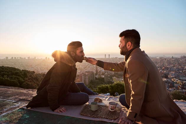 Man feeding croissant to boyfriend while sitting on observation point against city, Bunkers del Carmel, Barcelona, Spain model released Symbolfoto VEGF03670