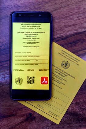 Eine mögliche Visualisierung des geplanten digitalen Impfpass liegt neben einem analogen Impfpass. Die EU-Staats- und Regierungschefs hatten am Donnerstag eine europäische Lösung beim Corona-Impfpass beschlossen. (Themenbild, Symbolbild)