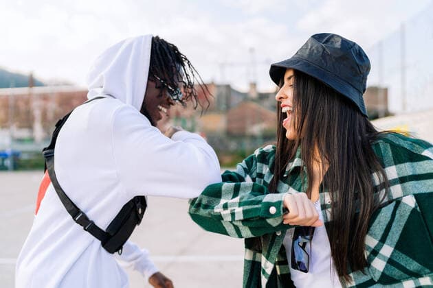 IMAGO Creative: Urban Diversity Young happy multiracial partners in trendy wear greeting each other with elbow bump on urban pavement Copyright: xLuisxManuelxMunozx Model Released