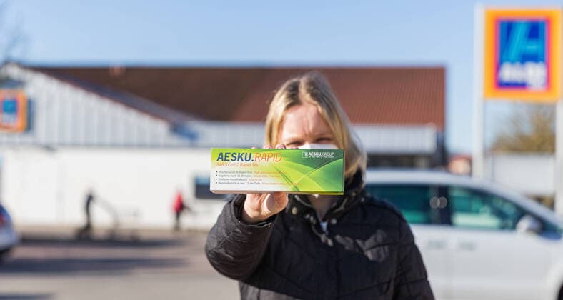 06.03.2021, Corona-Schnelltests bei Aldi: Ab heute verfügbar Bereits am heutigen Samstag bieten ALDI Nord und ALDI Süd sogenannte Corona-Antigen-Schnelltests Selbsttests zum Verkauf an. Drogeriemärkte wie Rossmann und Co ziehen am Montag nach. Eine Frau steht vor einer ALDI-Süd Filiale und hält einen AESKU.RAPID SARS-CoV-2 Rapid Test in der Hand. Bad Brueckenau Aldi Süd Bayern Deutschland