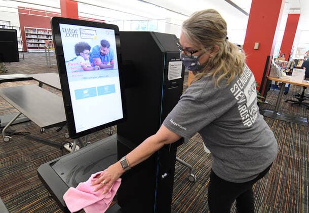 A worker sanitizes a check-out station at a public library in Plano, Texas on Tuesday, March 9, 2021. Texas Gov. Greg Abbott fully rescinded the statewide mask order and is allowing business to reopen at full capacity effective March 10, 2021 leaving organizations and businesses to determine if they want to require customers to wear masks or not.  DAL2021030907 IANxHALPERIN