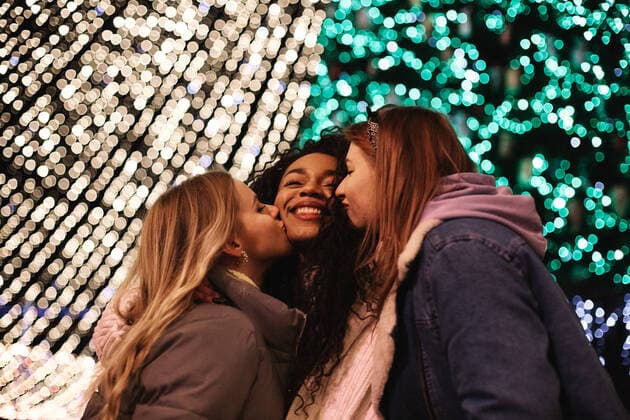 Diversity, Weihnachten Female friends kissing young woman on the cheeks by Christmas lights CR_DMBE210315-652179-01 ,model released, Symbolfoto