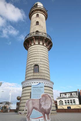 Blick am Donnerstag (18.03.2021) in Warnemünde auf den alten Leuchtturm mit dem Schriftzug Vorsicht Löwe im Mittelpunkt. Gegenwärtig sind in dem Ostseebad nur wenige Ausflügler zwischen dem Teepott und dem Hotel Neptun unterwegs. Dazu wirbt ein Aufsteller mit der Aufschrift Vorsicht Löwe für die Nutzung der Luca – App. Mit ihrer Hilfe kann das Gesundheitsamt die örtlichen Kontakte nachverfolgen. Dazu ist sie ein wichtiges Hilfsmittel zur Öffnung des Tourismus im Nordosten. Denn dieser steckt seit der Ausbreitung des Coronavirus nach wie vor in einer tiefen Krise. Dahingehend ist u.a. bisher völlig unklar, ob die Tourismusbetriebe wieder zu Ostern öffnen können. Eine Entscheidung dazu könnte jedoch am Montag (22.03.2021) beim Bund-Länder-Gip