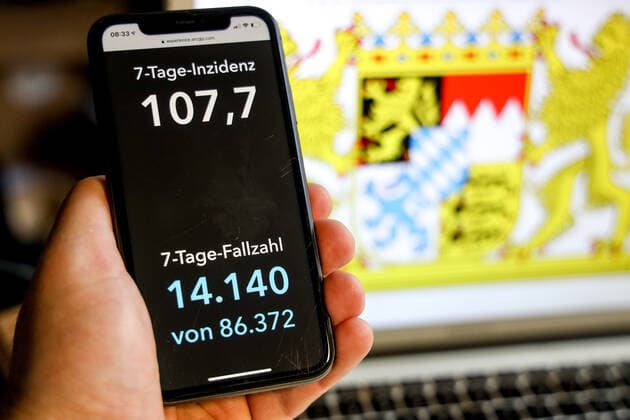 Coronavirus in Deutschland - Covid-19-Dashboard des Robert Koch-Institut DEU, Deutschland, Bayern, 21.03.2021: Die 7-Tage-Inzidenz für das Bundesland (Fälle letzte 7 Tage 100.000 EW) wird auf einem iPhone angezeigt, im Hintergrund das Landeswappen