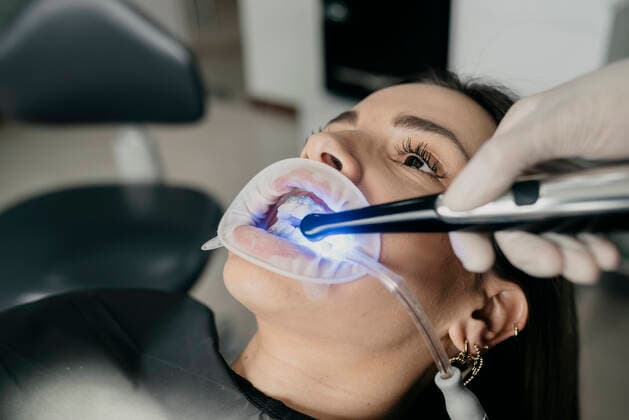 Crop unrecognizable dentist using dental curing light while treating teeth of female with saliva ejector and retractor in mouth, Model released Copyright: xDanielxSierraltax MR
