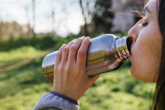 Side view of crop female hiker standing in forest and enjoying fresh water from metal bottle during hiking, Model released Copyright: xDavidxMunozx MR