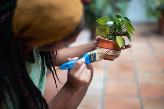 Cropped unrecognizable African American female gardener painting ceramic pot with Kalanchoe flower while working in hothouse, Model released Copyright: xNanoxCalvox MR