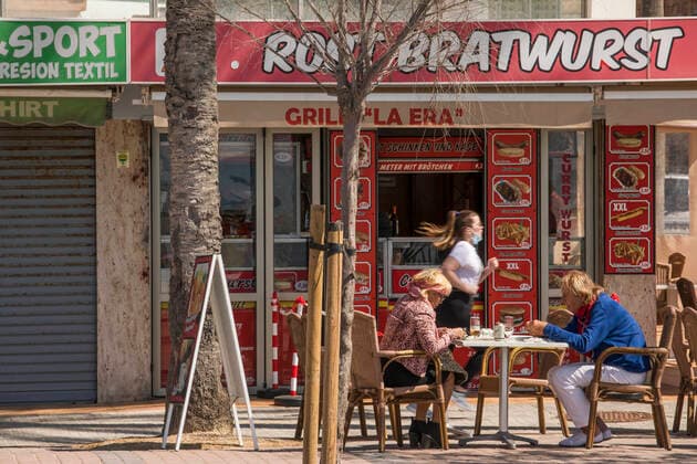 March 22, 2021, Mallorca, Spain: A couple sitting in the sausage restaurant Rostbratwurst with a woman running in the background at Playa de Palma in Mallorca. Spain - ZUMAm210 20210322_ztp_m210_001 Copyright: xJohn-PatrickxMorarescux