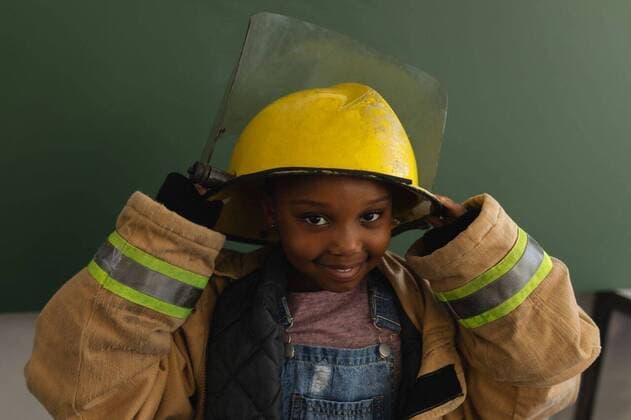 IMAGO Creative: Lokalhelden - Gesundheits- und Rettungskräfte Front view of black schoolgirl with fire uniform looking at camera in classroom Front view of a black schoolgirl with a too big fire uniform looking at camera in classroom of elementary school, model released, , property released, capetown, 28.01.2019, 1227926.jpg, school, elementary school, classroom, desk, bench, casual clothing, school kid, schoolgirl, student, classmate, chalkboard, standing, smiling, holding, looking, looking at camera, fire fighter, firefighting, uniform, pretending, aspirations, imagination, childhood, innocence, development, education, academic, information, knowledge, lifestyle, elementary, intelligent, intelligence, wisdom Child, Girl, Female, Black, 6-7 Years, Girls, African Ethnicity Indoors,Day
