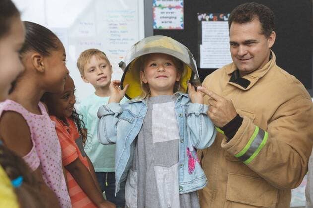 Firefighter teaching fire safety to school kids at school Front view of a Caucasian firefighter teaching to school kids about fire security while one of them has a fire helmet over her head, model released, , property released, Cork, Ireland, 05.02.2019, 1238541.jpg, school, classroom, desk, bench, uniform, casual clothing, fire helmet, school kid, schoolboy, schoolgirl, student, classmate, schoolteacher, schoolmaster, teaching, explaining, assisting, guidance, fire fighter, firefighting, pretending, aspirations, imagination, standing, holding, looking, talking, interacting, discussing, childhood, innocence, development, education, academic, information, knowledge, lifestyle, elementary, intelligent, intelligence, wisdom, together, group,