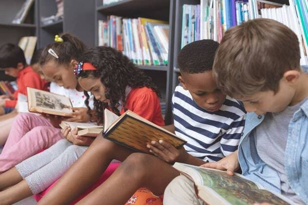 School kids sitting on cushions and studying over books in a library Side view of mixte ethnicity school kids sitting on cushions and studying over books in a library at school against bookshelfs in background, model released, , property released, Cork, Ireland, 05.02.2019, 1238586.jpg, school, library, books, book shelf, casual clothing, school kid, schoolboy, schoolgirl, student, classmate, study, studying, learning, sitting, holding, looking, talking, interacting, book, childhood, innocence, development, education, academic, information, knowledge, lifestyle, elementary, intelligent, intelligence, wisdom, together, group, friend, diversity Indoors,Front view