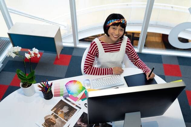 Female Graphic designer using graphic tablet Front view of young pretty Asian female graphic designer using graphic tablet at desk in office. This is a casual creative start-up business office for a diverse team, model released, , property released, Cape Town, South Africa, 17.03.2019, 1266679.jpg, graphic designer, artist, business, businesswoman, well dressed, executive, associate, occupation, profession, professional, skill, expertise, creative, entrepreneur, corporate, company, office, workplace, desk, color swatch, color shade, cup, coffee, spectacle, sitting, working, looking, editing, graphic tablet, digitizer, graphic, stylus, mobile phone, wireless technology, computer, desktop pc, electronic, personal computer, keyboard, connecti