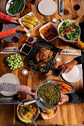 Millennial adult friends celebrating Thanksgiving together at home Overhead view of a group of young adult multi-ethnic male and female friends sitting around a table holding dishes and serving Thanksgiving dinner at home together, model released, , property released, Cape Town, South Africa, 10.09.2019, 1289456.jpg, friends, friendship, socialising, free time, spare time, home, apartment, dining room, domestic life, together, enjoying, hands, relaxing, gen z, generation z, thanksgiving, holidays, tradition, celebrating, celebration, food, meal, dinner, festive, festivity, serving, sharing, passing, holding, dish, sitting, roast dinner, salad, vegetables, lunch, dinner party, roast turkey, table, plate, wine, wine glass, candle Young Adult