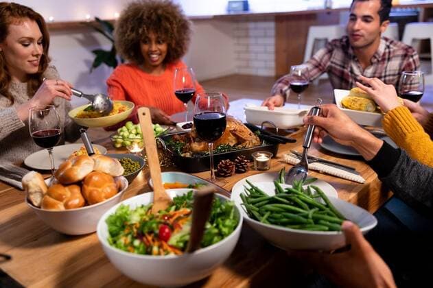Millennial adult friends celebrating Thanksgiving together at home Front view of a group of young adult multi-ethnic male and female friends sitting around a table holding dishes and serving Thanksgiving dinner at home together, model released, , property released, Cape Town, South Africa, 10.09.2019, 1289457.jpg, friends, friendship, socialising, free time, spare time, home, apartment, dining room, domestic life, together, enjoying, happy, smiling, hands, relaxing, gen z, generation z, thanksgiving, holidays, tradition, celebrating, celebration, food, meal, dinner, festive, festivity, serving, sharing, passing, holding, dish, sitting, roast dinner, salad, vegetables, lunch, dinner party, roast turkey, table, plate, glass, candle, wine, re