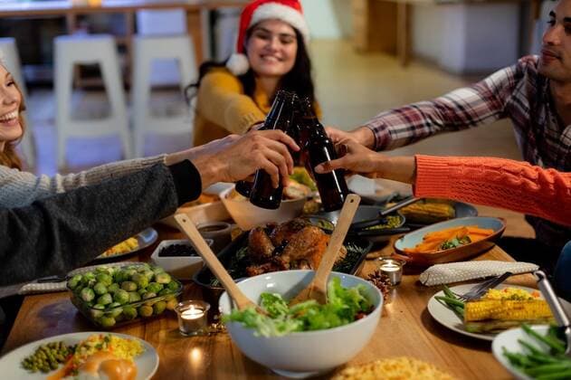 Millennial adult friends celebrating Christmas together at home Side view of a group of young adult multi-ethnic male and female friends sitting at a table at home set for Christmas dinner making a toast with bottles of beer, one woman is wearing a Santa hat, model released, , property released, Cape Town, South Africa, 10.09.2019, 1289469.jpg, friends, friendship, socialising, free time, spare time, home, apartment, domestic life, together, enjoying, happy, smiling, relaxing, gen z, generation z, christmas, xmas, yuletide, holidays, celebrating, celebration, festive, festivity, tradition, food, meal, sharing, roast dinner, vegetables, lunch, dinner, dinner party, roast turkey, making a toast, raising, holding, beer, bottle, drinking, san