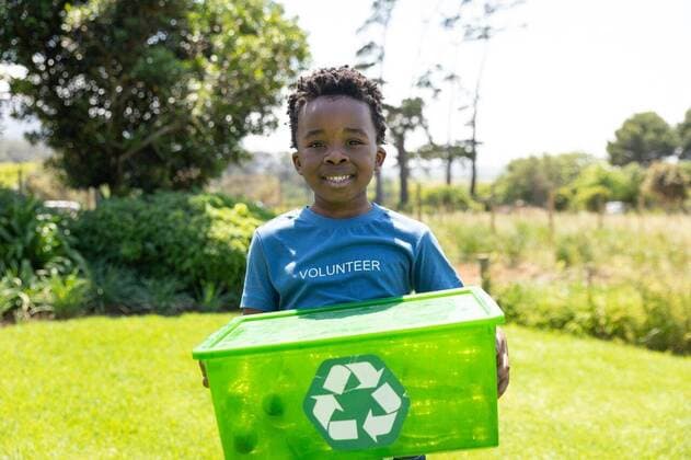 IMAGO Creative: Klimawandel - Umwelterziehung Volunteers collecting rubbish and recycling Front view of a smiling young African American boy standing in a field wearing a t shirt with volunteer written on it, holding a green plastic recycling crate and smiling to camera, model released, , property released, Cape Town, South Africa, 17.11.2019, 1297934.jpg, people,real people,home,domestic life,lifestyle,free time,leisure,relaxing,happy,enjoying,childhood,summer,nature,field,recycling,eco-friendly,green,volunteer,volunteering,environment,cleaning,awareness,education,learning,social responsibility,community,community spirit,helping,rubbish,collecting,trash,rural,countryside Child,Boy,Male,Black Outdoors,Front view,Close-up,Copy space,Looking at camera,Day,Half length