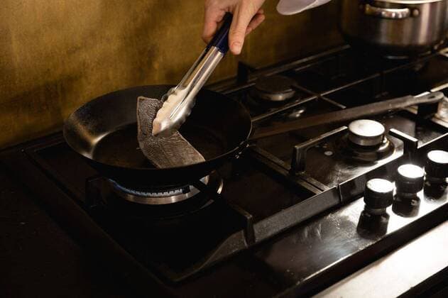 IMAGO Creative: Clickbait, Rezepte und Kochen Chef cooking a fish Close up of a Caucasian person at a cookery class, frying fish on a frying pan. Active Seniors enjoying their retirement., model released, , property released, Cape Town, South Africa, 05.12.2019, 1317576.jpg, people,fresh,fish,pan,frying,cooking,work station,chefs whites,uniform,counter top,real people,restaurant,business,food,kitchen,cookery,cuisine,culinary,catering,profession,job,experience,skill,busy,service,professional,confident,work,worker,working,preparation,preparing,making,chef,head chef,class,training,student,teacher,teaching,learning,education,workshop,cook Young Adult,Woman,Female,Caucasian Indoors,Day