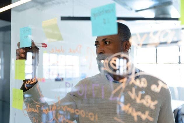 African American man writing on sticky notes Front view close up of a mixed race man working in a modern office, writing on a paper stick on a glass board. Social distancing and self isolation in quarantine lockdown, model released, , property released, Cape Town, South Africa, 12.10.2019, 1330111.jpg, social distancing, alone, quarantine, self isolation, real people, isolation, distance, lock down, people, creative, business, design professional, profession, professional, job, career, occupation, work, working, agency, company, creativity, casual, design, designer, start up, new business, entrepreneur, studio, office, workplace, modern, brainstorm, brainstorming, writing, glass wall, thinking, inspiration, information, logistics, strategy