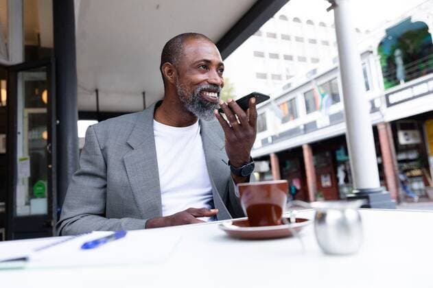 African American man having a phone call at coffee terrace African American man spending time at cafe, sitting at a coffee terrace, having a cup of coffee and talking on his smartphone., model released, , property released, Cape Town, South Africa, 11.03.2020, 1334669.jpg, people,real people,commuting,commuter,travel,city,creative,individuality,lifestyle,street fashion,modern,on the go,digital nomad,independent,casual,street,cafe,table,coffee terrace,coffee,beverage,cup,smartphone,mobile phone,technology,phone,holding,using,communication,connection,interacting,on the phone,phone call,talking,smiling,social distancing Mature Adult,Man,Male,Black Outdoors,Side view,Day,Half length